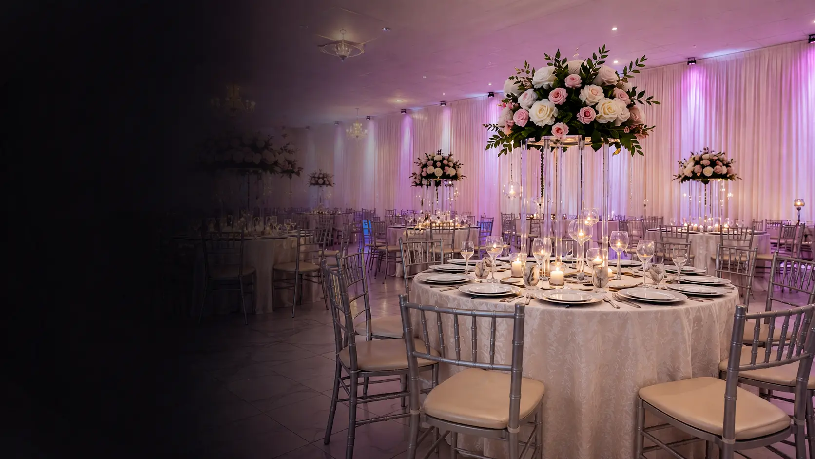 The La Orquídea ballroom set for a reception — round tables with candles, tall pink rose centerpieces, white draped walls, and pink-violet uplighting