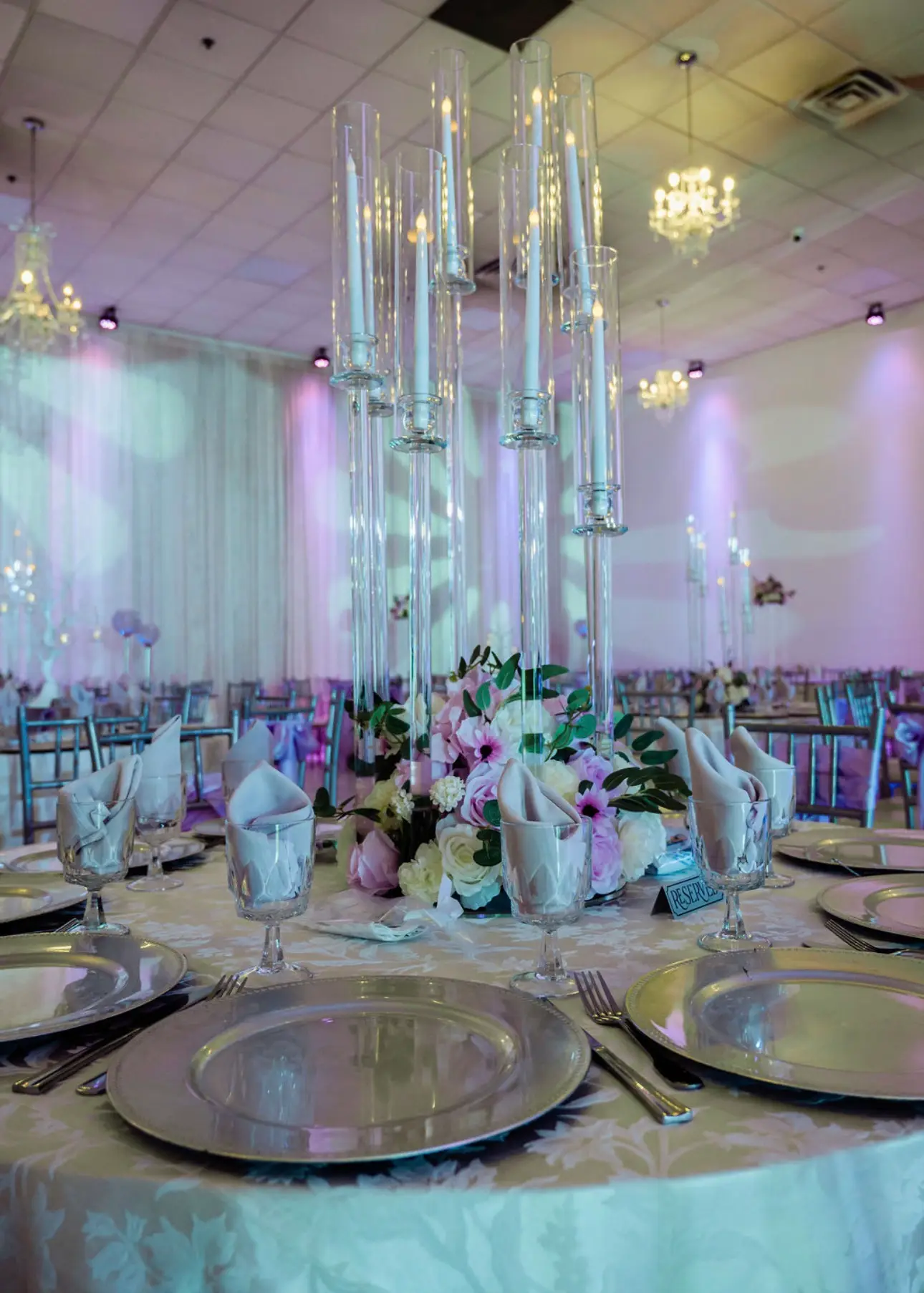 Reception table in blush and ivory with a tall crystal candelabra centerpiece of roses and orchids, patterned lighting on the dance floor behind