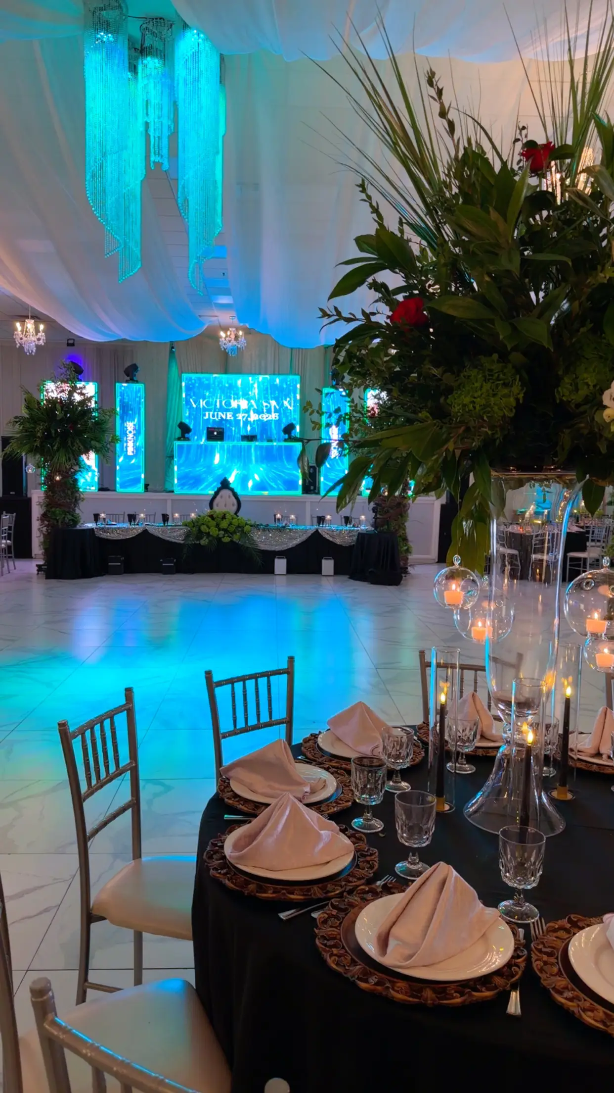 Head table and dance floor framed by greenery and black drapery, with a glowing LED screen backdrop