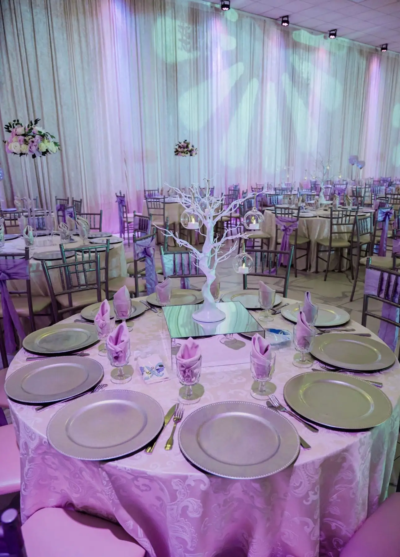 Quinceañera table in lilac with silver chargers and a white branch centerpiece hung with ornaments
